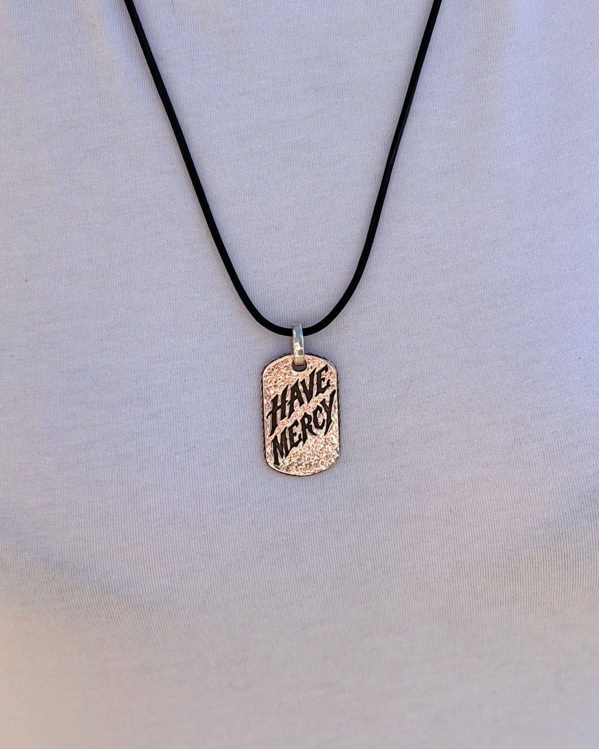 Woman wearing the Have Mercy sterling silver pendant on a black leather cord over a white t-shirt, front view
