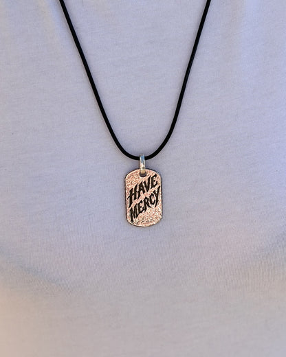 Woman wearing the Have Mercy sterling silver pendant on a black leather cord over a white t-shirt, front view