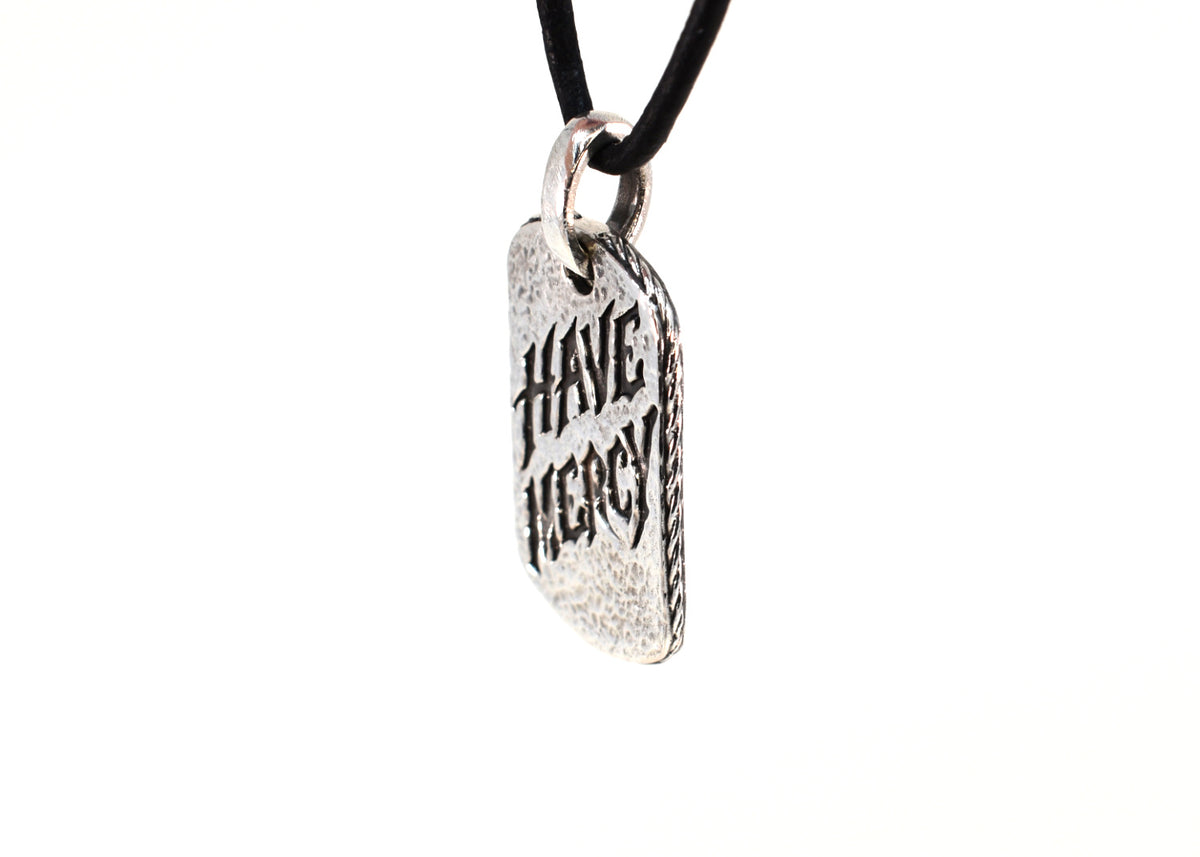 Angled view of Have Mercy pendant hanging on black leather cord