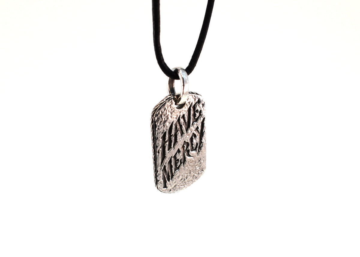 Three-quarter view of Have Mercy pendant hanging on black leather cord
