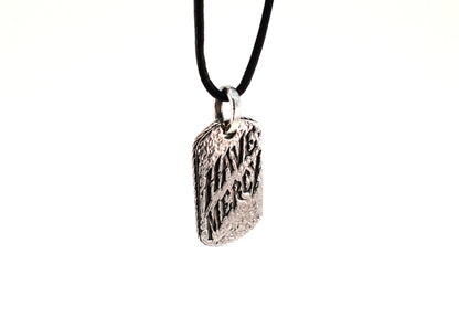 Three-quarter view of Have Mercy pendant hanging on black leather cord